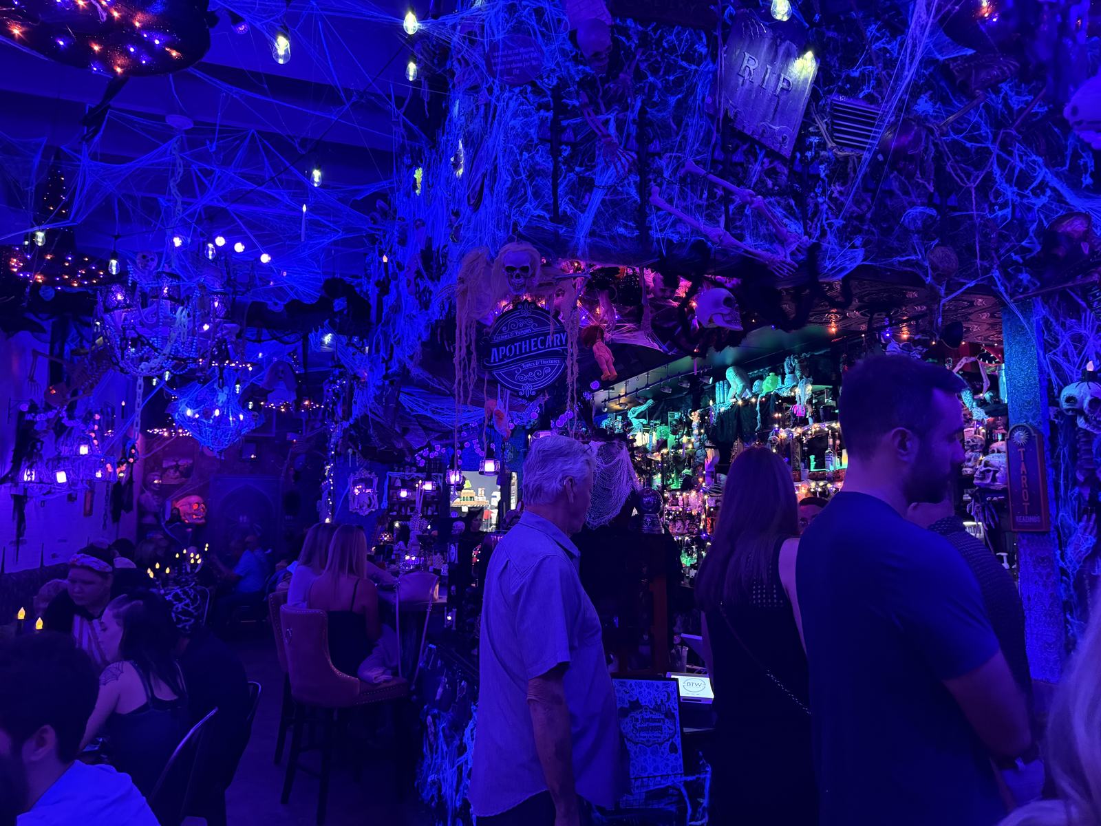 Cobwebs and Halloween decorations over the bar and seated guests under purple lighting at BTW Spookeasy in Tavares.