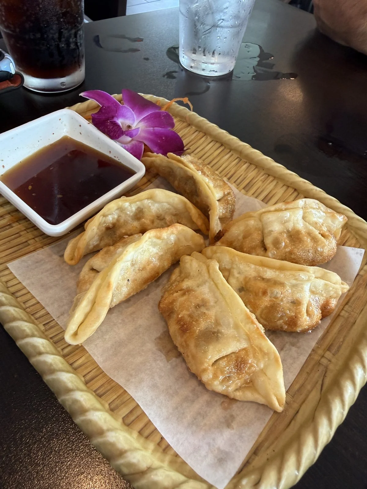 Fried dumplings in a basket with dipping sauce and an orchid garnish at Kumo Sushi & Hibachi.
