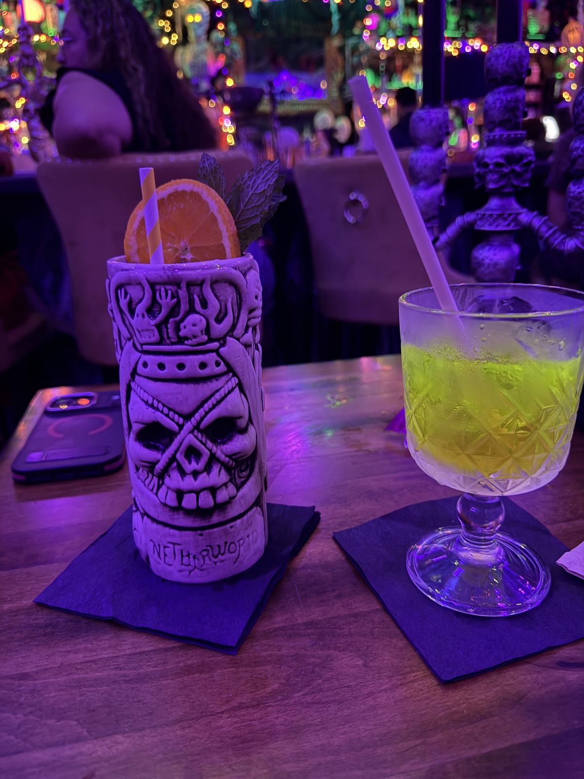 Skull-themed cocktail cup beside a yellow-green drink on the bar at BTW Spookeasy.