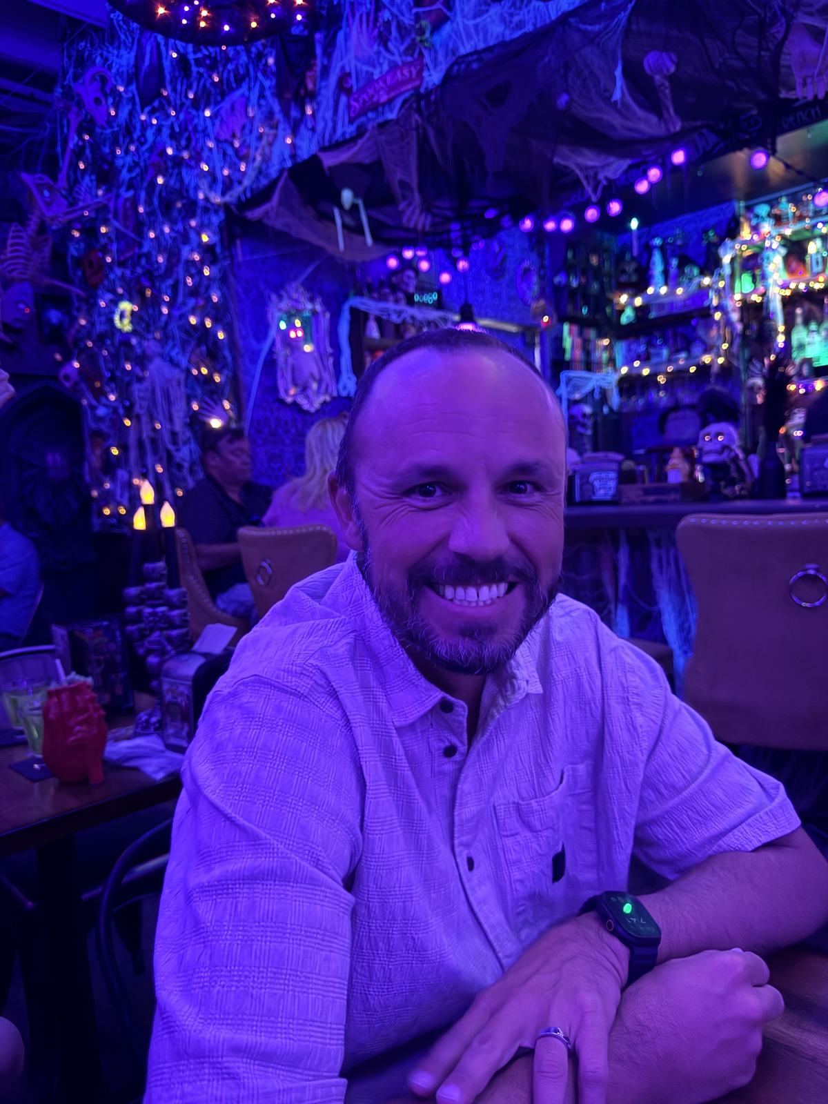 Jason seated at BTW Spookeasy with purple lighting and hanging Halloween decorations behind him.