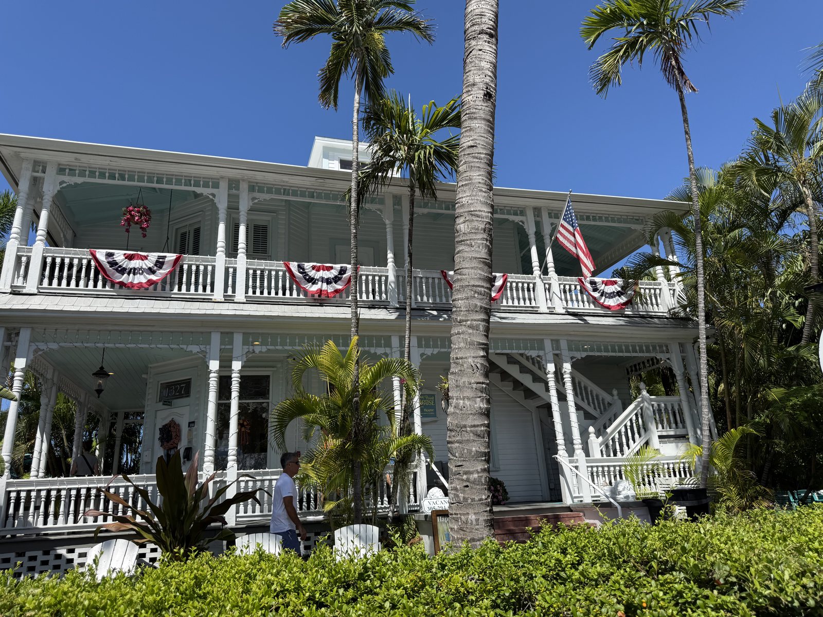 White Key West guesthouse with two-story porches, palm trees, and red, white, and blue bunting.