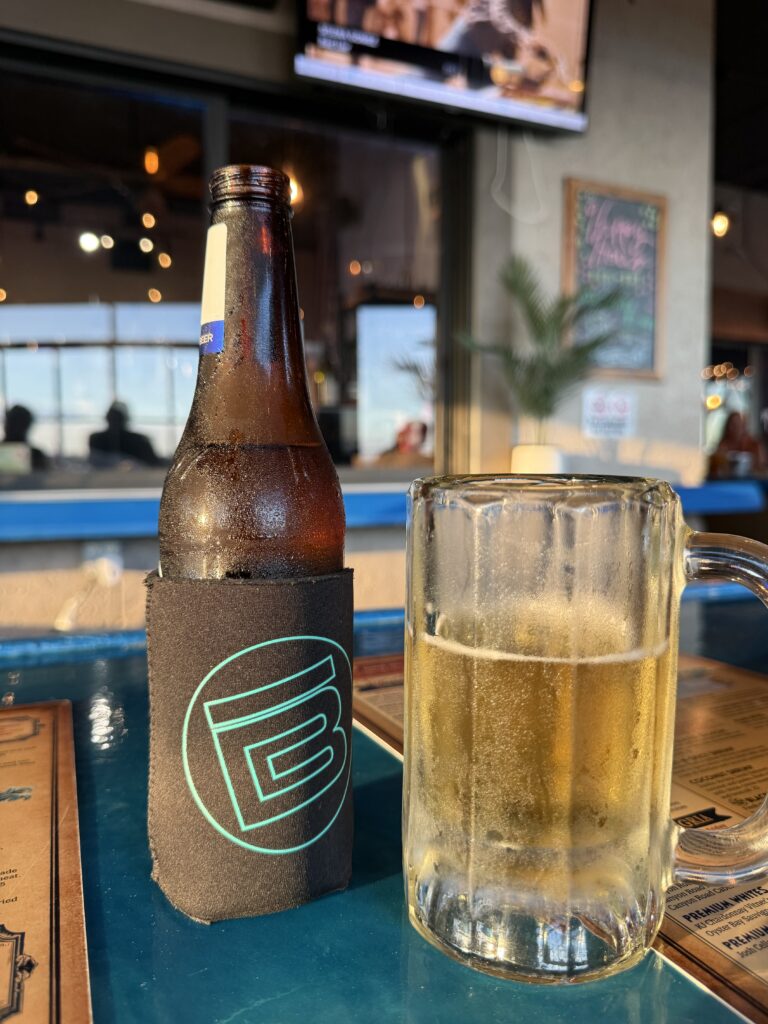 Cold beer bottle in a koozie beside a frosty glass mug of beer at Puddle Jumpers