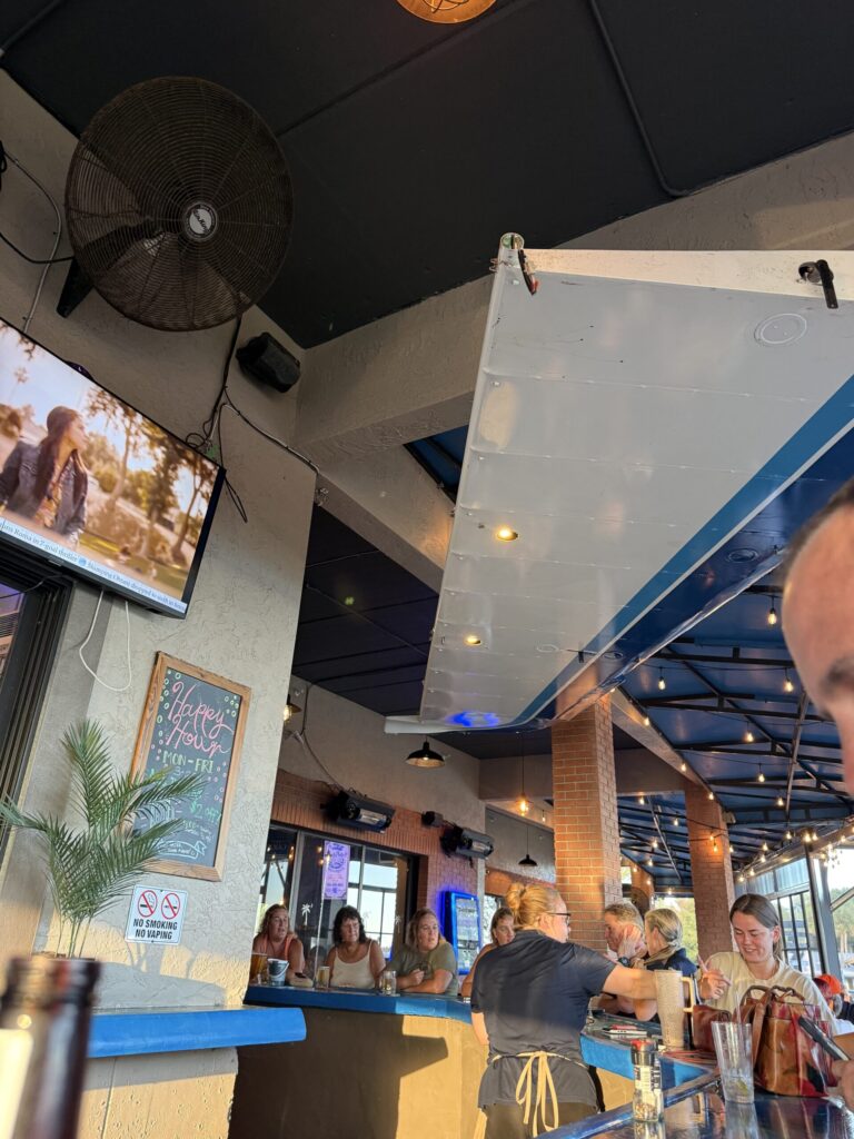 Interior of Puddle Jumpers bar in Tavares with guests, a ceiling-mounted airplane wing and blue countertops