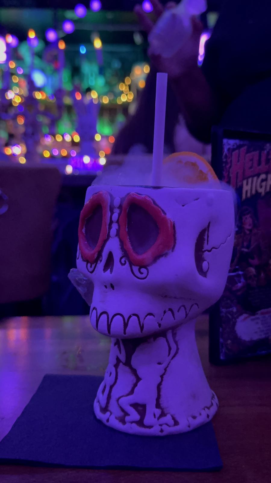 White skull-shaped cocktail cup with red eye sockets, orange garnish, and a straw at BTW Spookeasy.