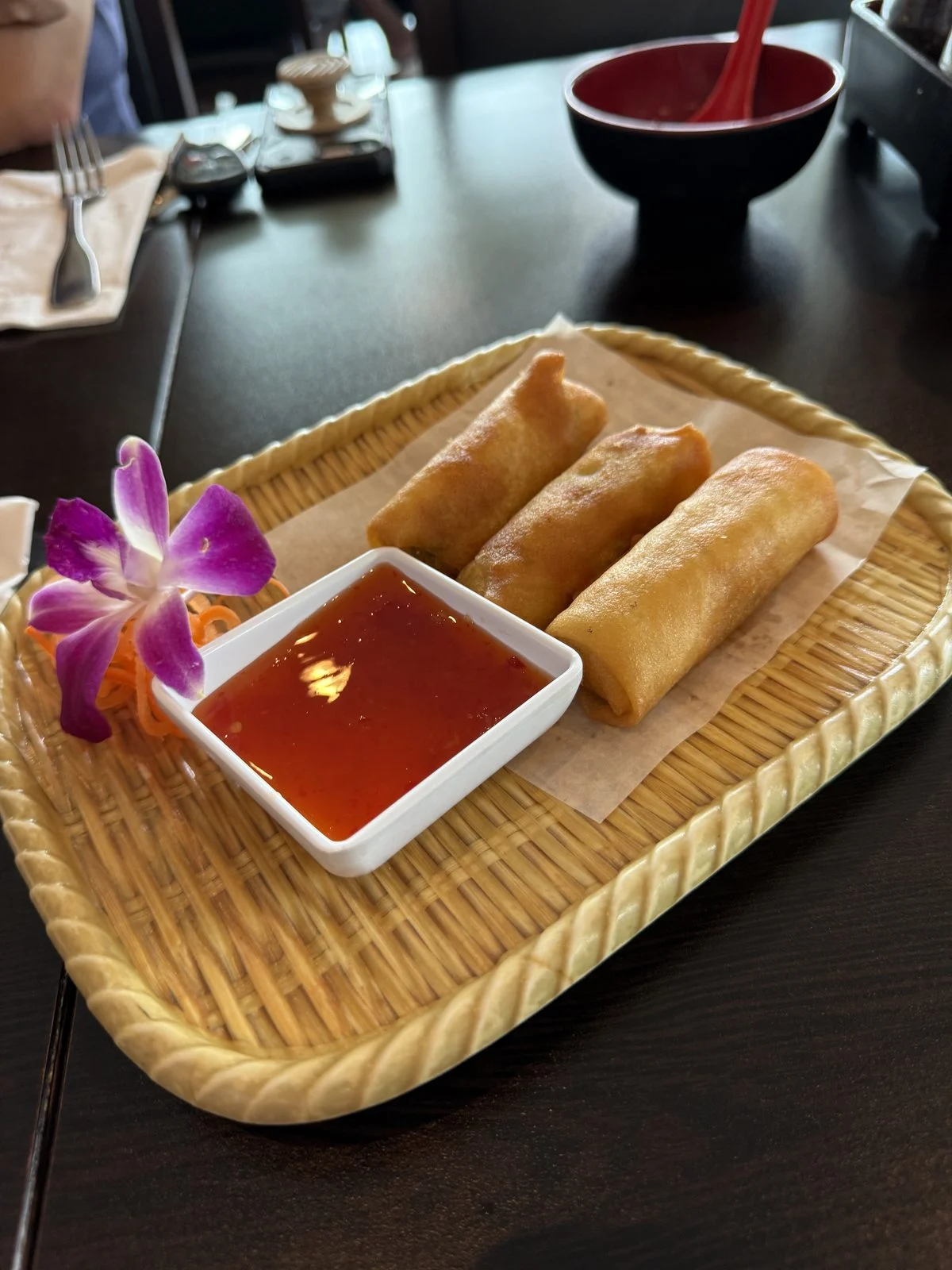 Three golden spring rolls with red dipping sauce and an orchid garnish at Kumo Sushi & Hibachi.