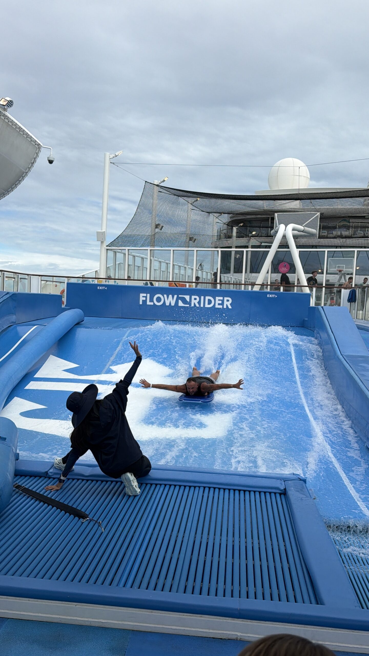 Person falling forward on the FlowRider surf simulator as an instructor watches